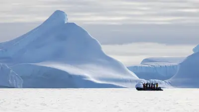 Zodiac cruising beside a towering iceberg